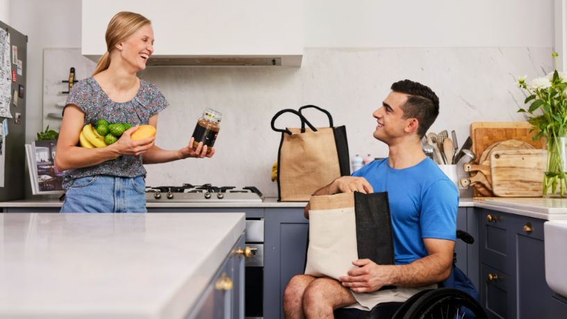 Two people unpack food shopping in their kitchen.