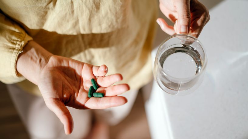 A person holds vitamins in one hand and a glass of water in the other.