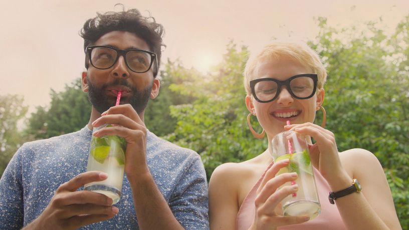 2 people smiling with drinks in a glass using a straw