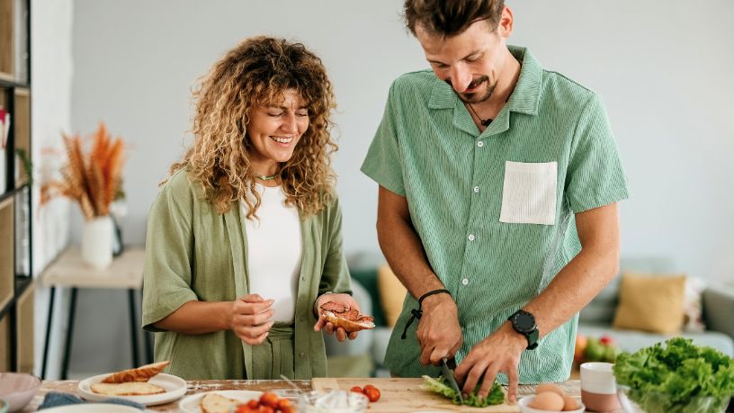 Two people smile as they slice veggies for their lunch.