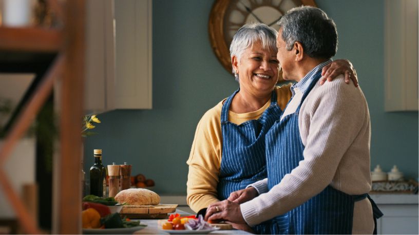 An older couple laugh while chopping vegetables for their lunch.