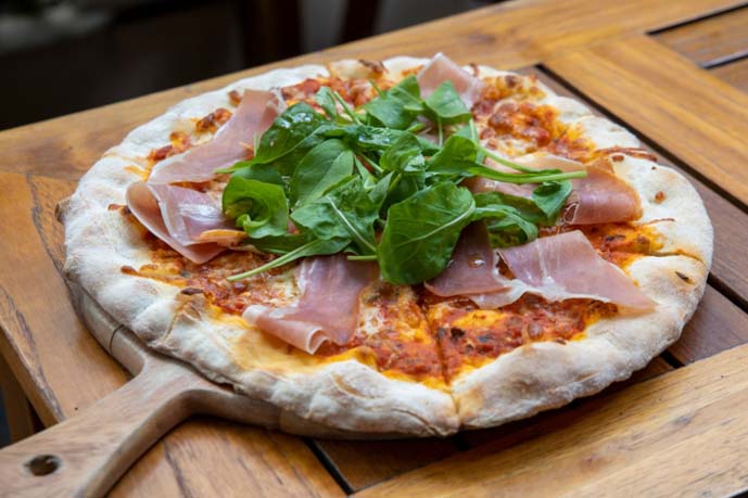 Pizza with a pita base, tomato sauce, some greens and ham.