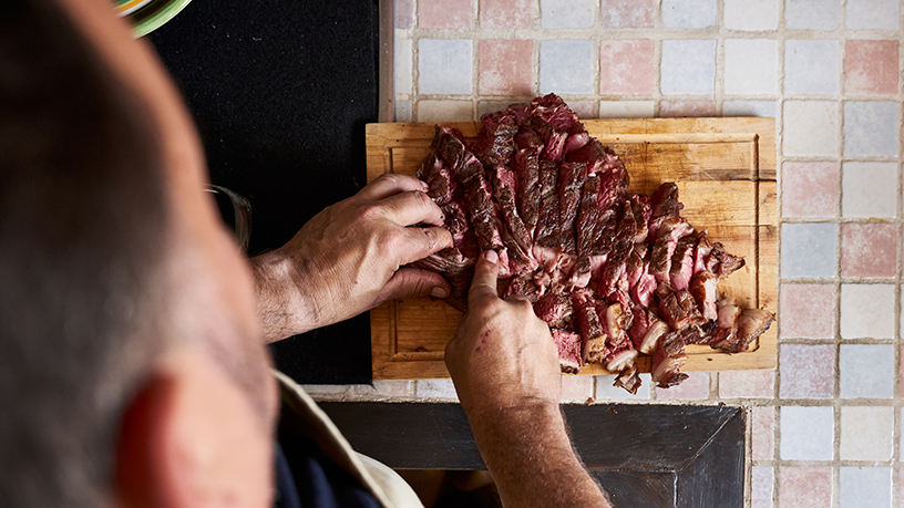 A man cutting up a large piece of meat.