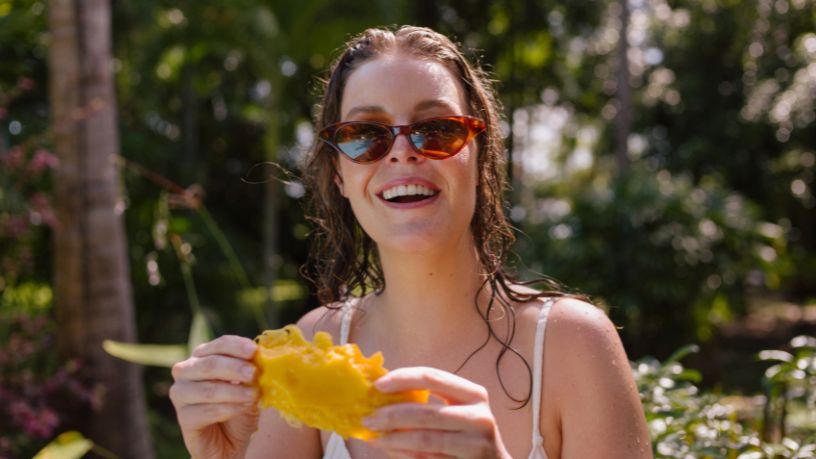 A woman smiles while eating a mango.