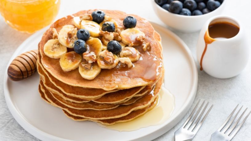 A plate of banana power pancakes sits on a table next to various accompaniment.