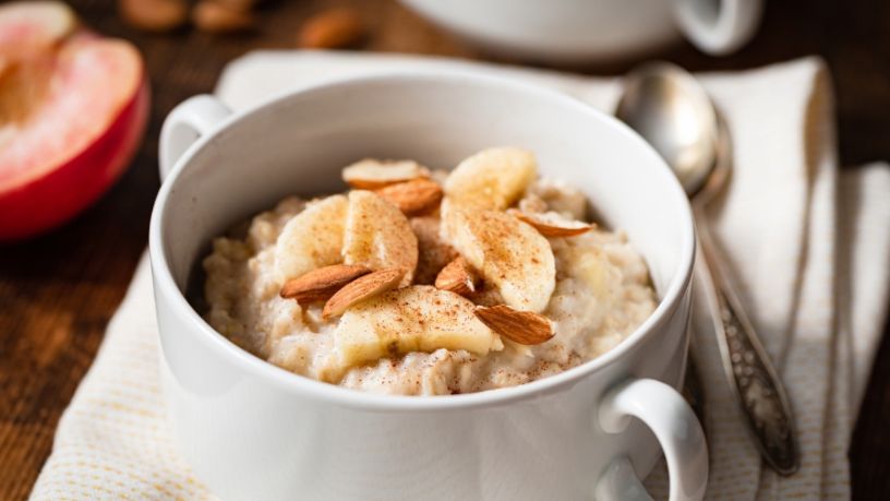 A bowl of breakfast oats is topped with banana slices and almonds.