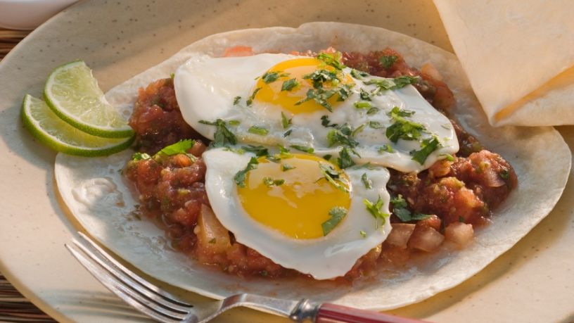 A plate of huevos rancheros sits on a dining table.