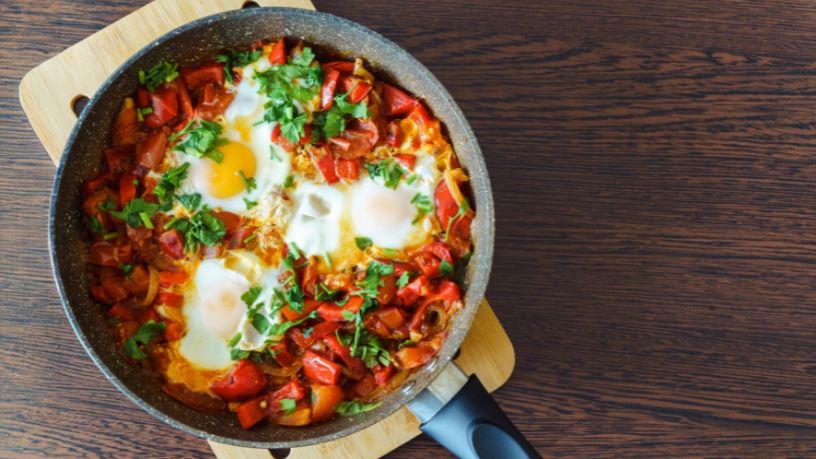 A pan filled with various breakfast ingredients rests on a chopping board.