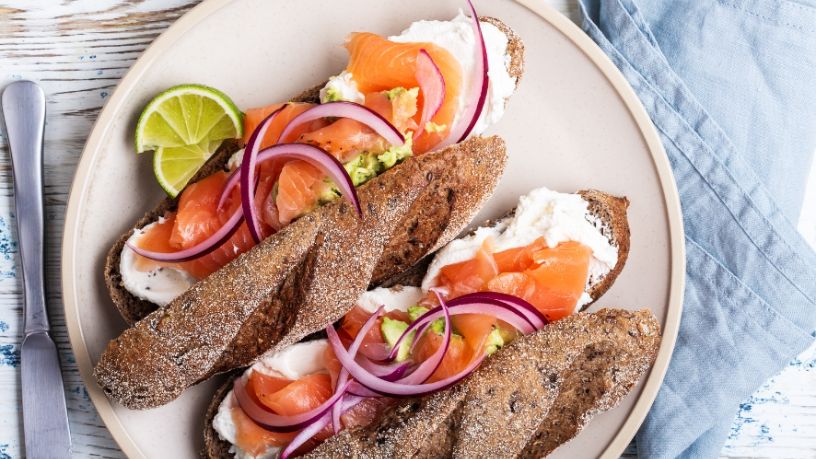 A plate is filled with ricotta and avocado smash with smoked salmon in rye bread rolls.