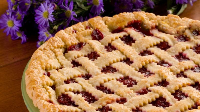 Baked pastry tart with pastry lattice decoration on a table with purple flowers