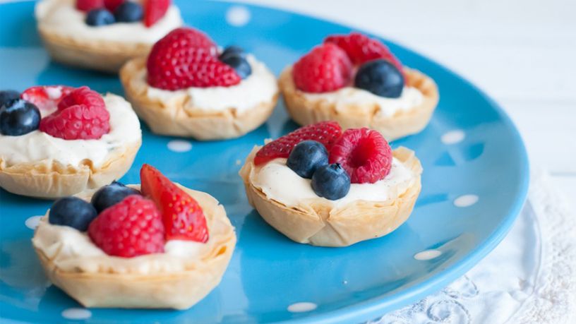 Small tarts topped with yoghurt and berries on a blue plate