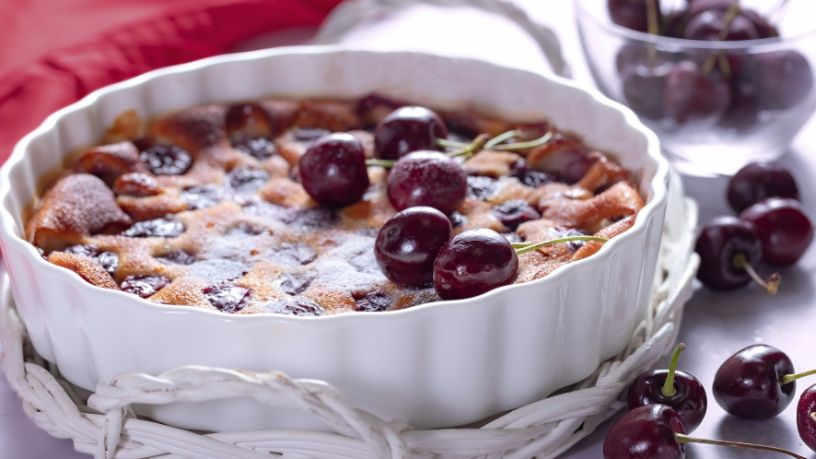 Baked cherry tart in a white dish topped with fresh cherries