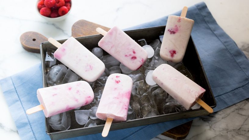 Pink and white ice creams on sticks laying on a tray of ice cubes
