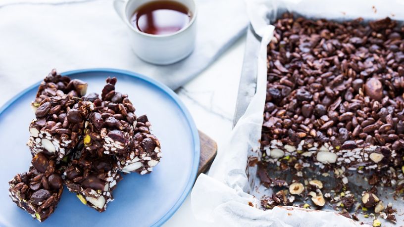 Tray of chocolate rocky road with chunks of nuts next to plate of rocky road slices