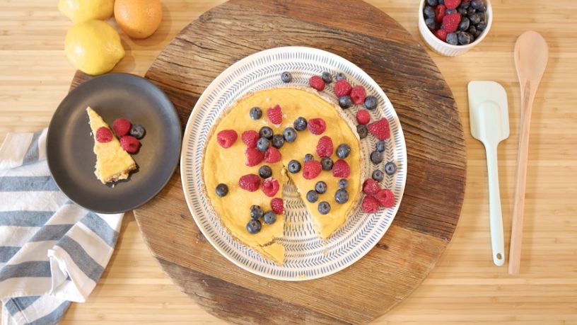 Plated lemon tart topped with blueberries and raspberries on a wooden table