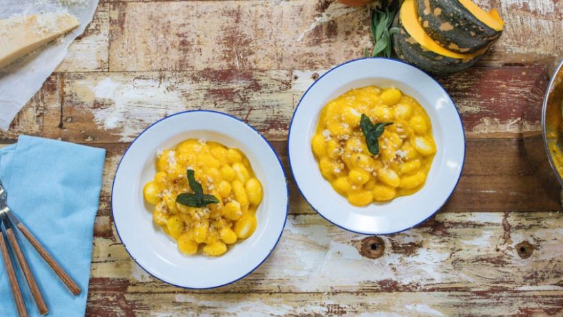 Two bowls of pumpkin, sage and pine nut gnocchi sit on a rustic dining table