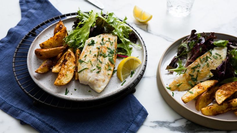 Two plates of grilled fish and chips sit on a table