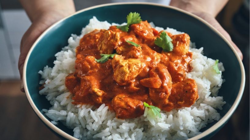 A person holds a bowl of yellow chicken curry and cauliflower rice.