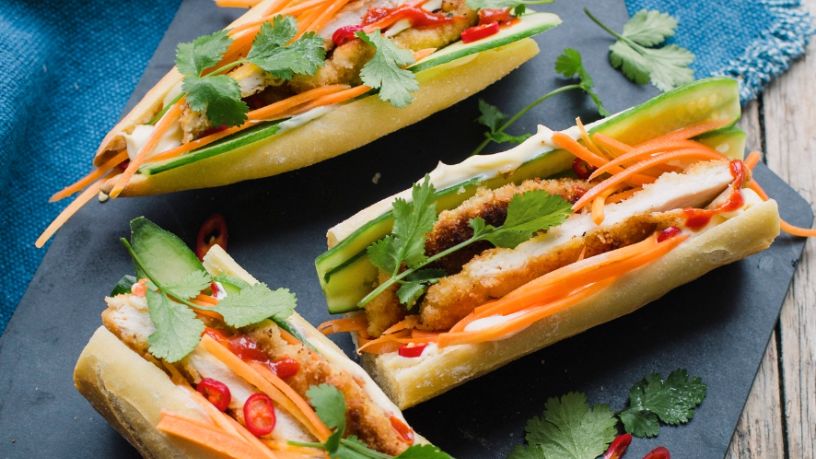 Three bahn mi sandwiches lay side by side.