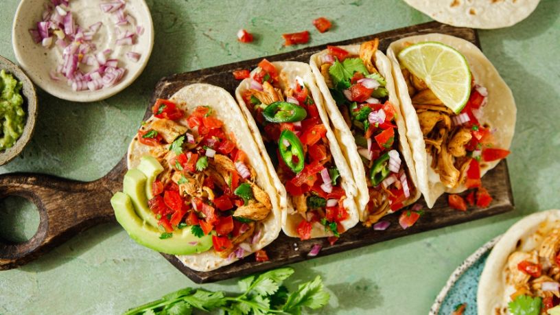 Four chicken tacos are arranged onto a serving board.
