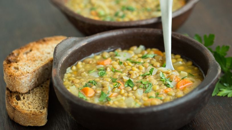 Two bowls of lentil soup sit on a table alongside slices of toast.