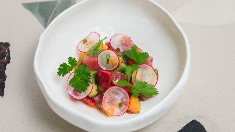 Mix of fish and vegetables topped with radish slices and parsley in a white bowl.