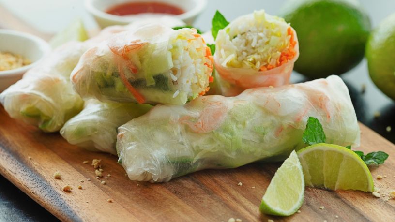 Rice paper rolls filled with vermicelli, prawns and vegetables on a wood platter with lime.