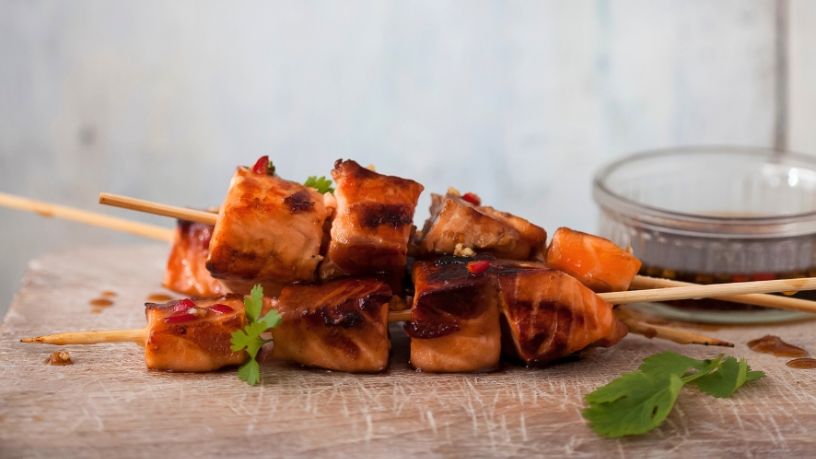 Grilled salmon skewers with parsley on a wood platter.