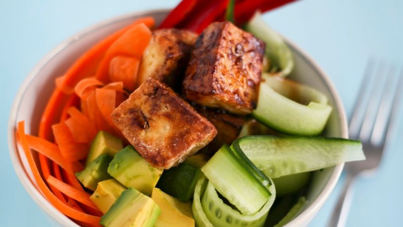 Bowl filled with cucumber, carrot, avocado, capsicum and fried tofu cubes.