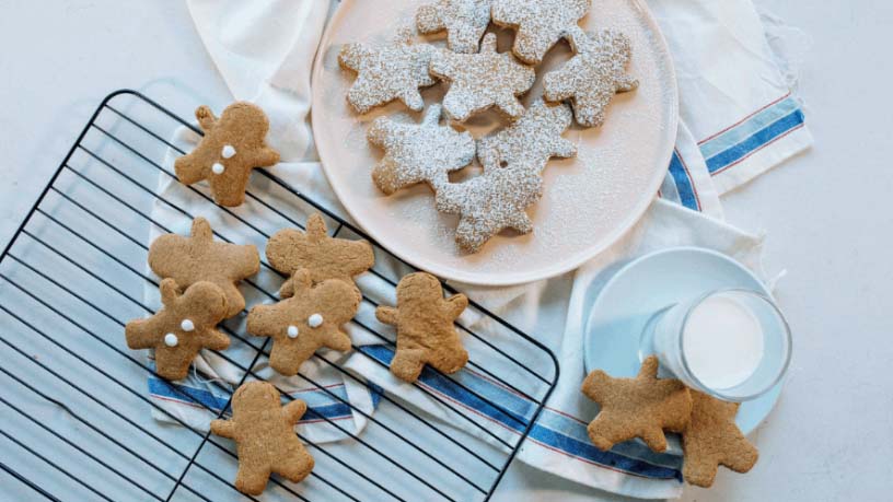 Several gingerbread biscuits lay on a table alongside a glass of milk.