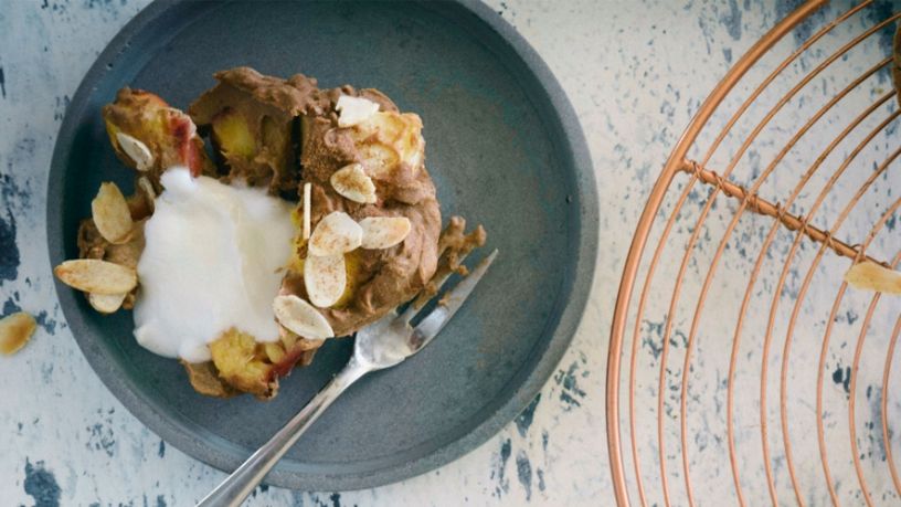 A nectarine and date muffin sits in a bowl with a side of yoghurt.