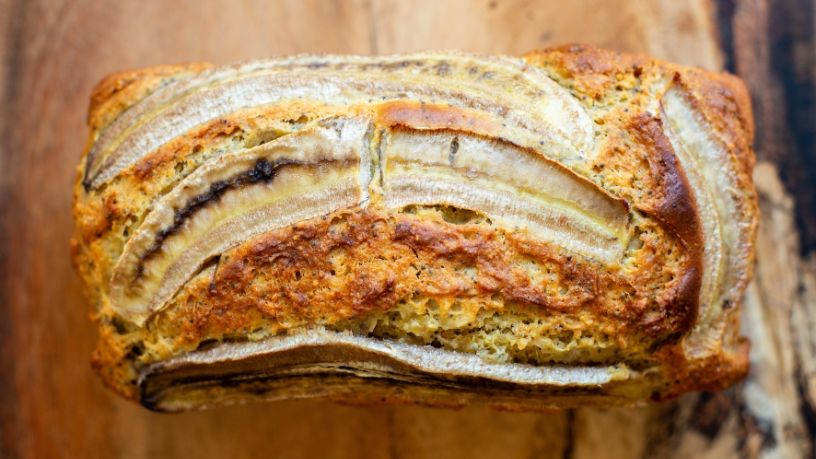 A loaf of banana bread rests on a rustic wooden bench.