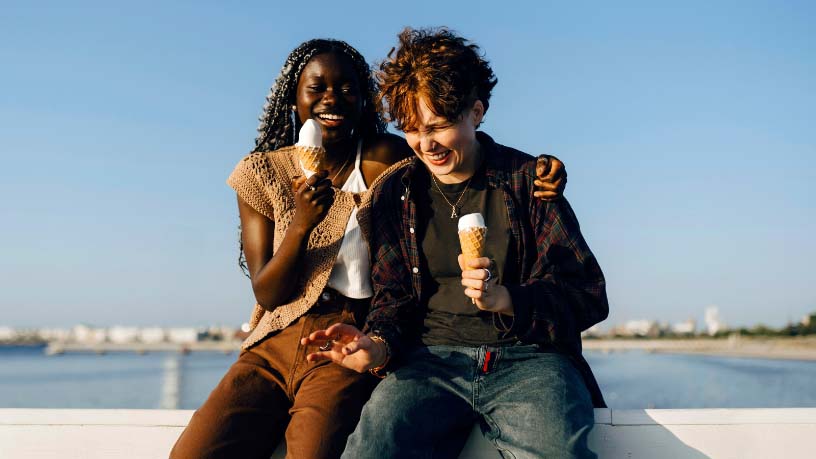 Two people eat ice creams by the water.