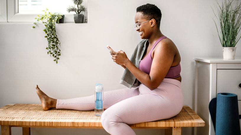 A woman looks at her phone and smiles after a workout. 