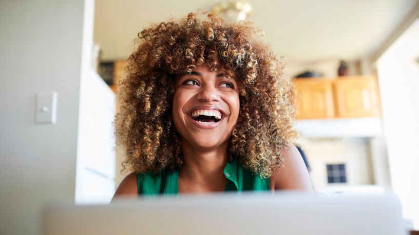 A woman smiles while sitting in front of her laptop.