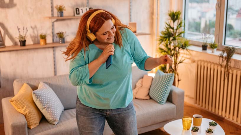 A woman wearing headphones dances in her living room.