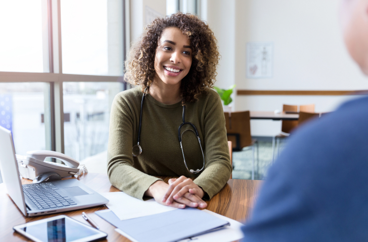 A doctor with a stethoscope around their neck smiling at a patient sitting opposite them