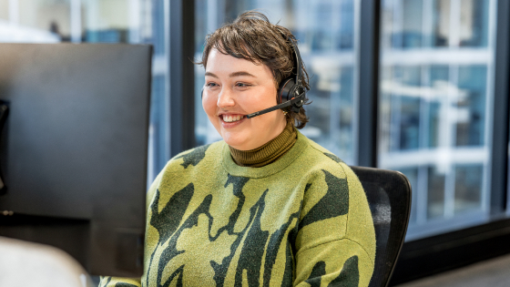 A smiling customer representative behind a computer with a headset on