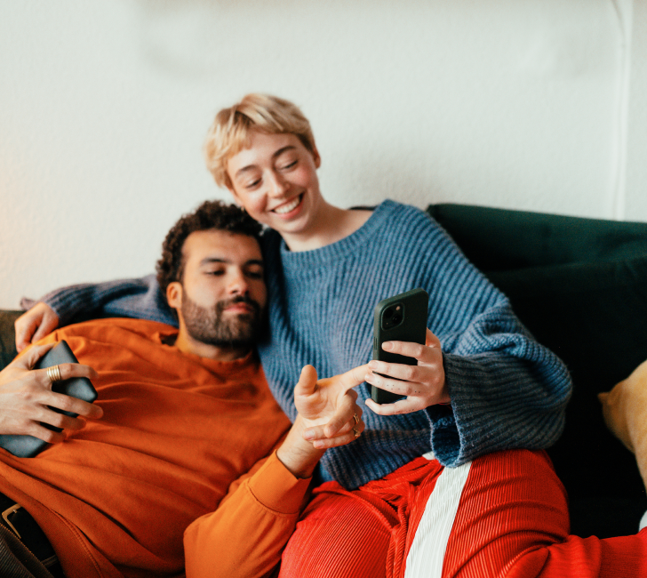 A young couple relaxing together on a couch, sharing a moment looking at a phone.